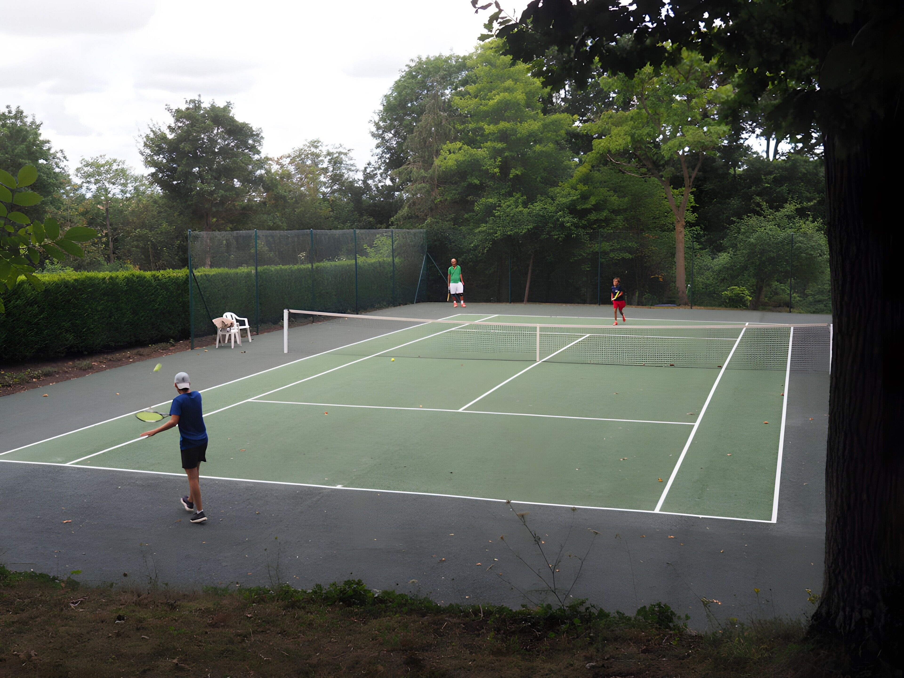An outdoor tennis court with a net, surrounded by trees and a fence.