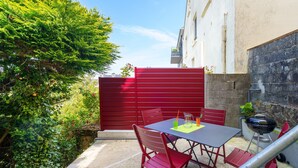 Un patio con mesa y sillas, una parrilla y un portón rojo.
