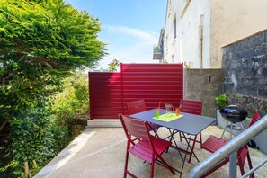 Eine Terrasse mit Tisch und Stühlen, einem Grill und einem roten Tor.