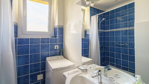 Un baño con azulejos azules, una ventana, un inodoro, un lavabo y una ducha.