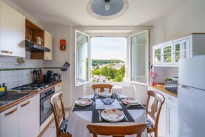 Una cocina moderna con ventana abierta, mesa de comedor lista para cuatro personas y vistas a un pueblo.