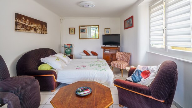 Habitación de hotel con una cama, dos sillones, un sofá, un televisor, una ventana con persianas y un cuadro en la pared.