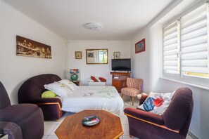 A hotel room with a bed, two armchairs, a sofa, a TV, a window with blinds, and a painting on the wall. - La Korrigane - À 1,5 km de la plage (Douarnenez)