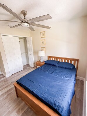 Un dormitorio con cama, ventilador de techo, mesita de noche, lámpara y puerta que da a un armario.
