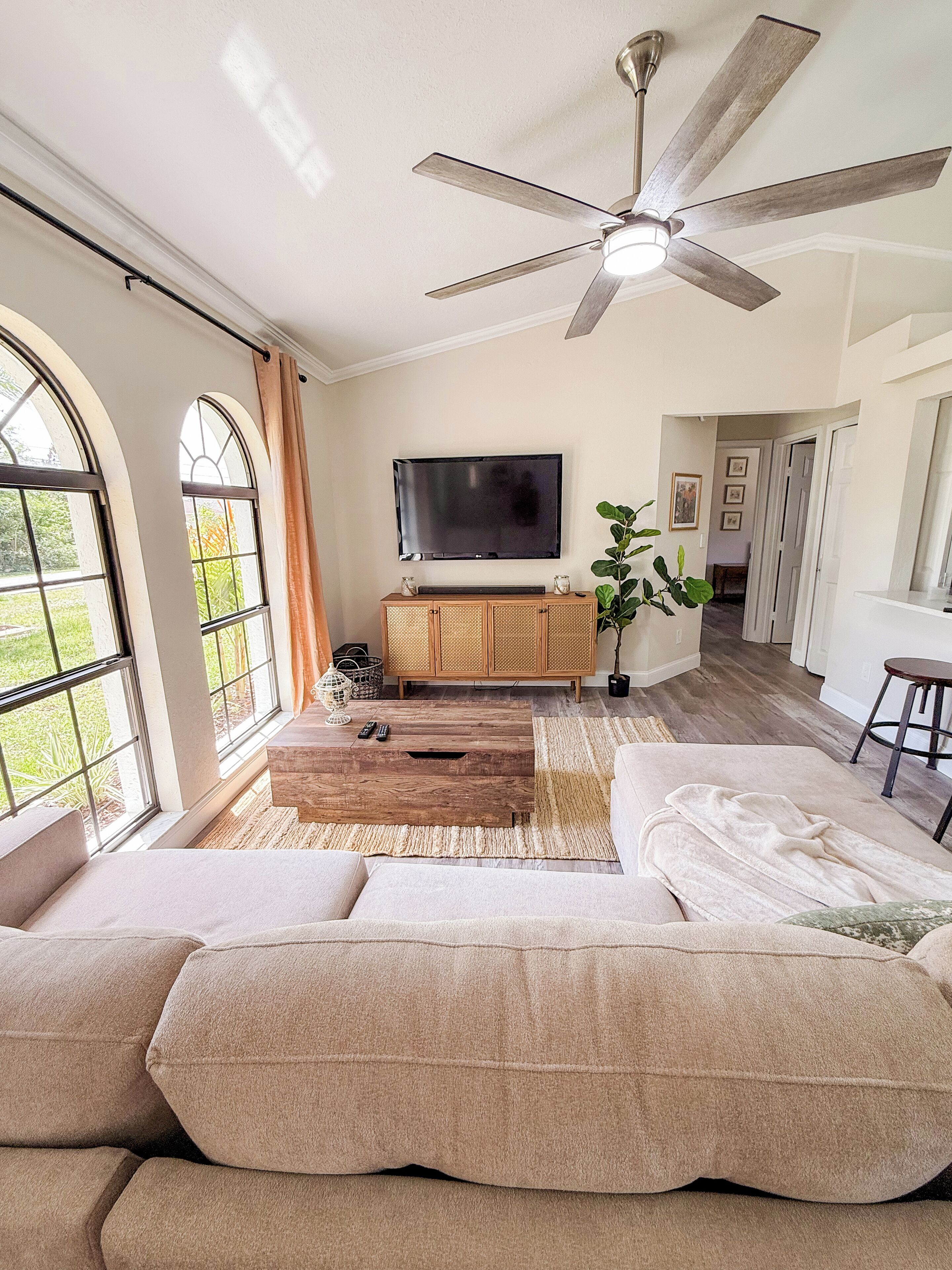 A living room with a large sofa, a wooden entertainment unit, a ceiling fan, and a flat-screen TV.