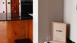 Una cocina moderna con horno empotrado y microondas, un banco de madera y una pequeña mesa blanca con un cuadro enmarcado.