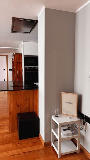 Eine moderne Küche mit Einbauofen und Mikrowelle, einer hölzernen Bank und einem kleinen weißen Tisch mit einem gerahmten Bild.