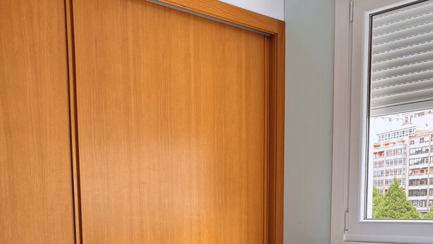 Un dormitorio con un armario de madera, una cama con ropa de cama blanca y una ventana con persianas.