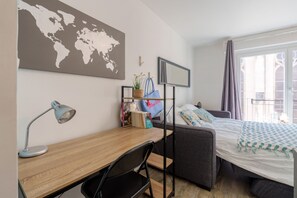 Ein ordentlich eingerichtetes Schlafzimmer mit einem Bett, einem Schreibtisch mit Lampe, einer Weltkarte an der Wand und einem Fenster mit Vorhängen.