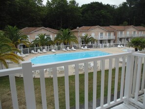 Ein Schwimmbecken mit Liegestühlen, umgeben von einem weißen Zaun, und eine Reihe von Gebäuden im Hintergrund.