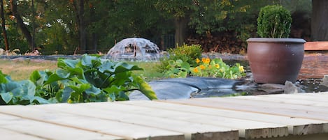 Ein Garten mit einem Wasserspiel, einer Holzterrasse und einem großen Pflanzgefäß.
