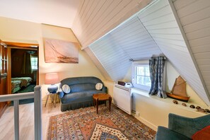 A cozy attic room with a sloped ceiling, a blue sofa, a patterned rug, and a small wooden table. - Ty Crugo - Jolie maison familiale avec jardin (Saint-Lyphard)