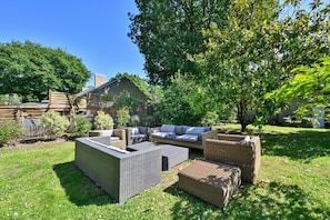 A patio with wicker furniture, a wooden fence, and a large tree. - Ty Crugo - Jolie maison familiale avec jardin (Saint-Lyphard)