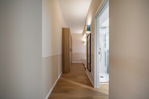 A narrow hallway with wooden flooring, a tall wooden cabinet, and a glass door leading to a bathroom. - Cozy luxury apartment in the city centre (Parma)