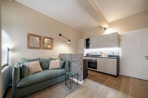 Ein kompakter Wohnbereich mit Sofa, kleinem Tisch, Küchenzeile mit Schränken und Herd, sowie einer Tür.