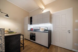 Une cuisine compacte dotée d’un four encastré, d’un plan de travail noir et d’une porte blanche.