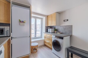 A compact kitchen with a microwave, washing machine, and wooden cabinets. - L’éclat de Baccarat - Maison cosy en triplex (Baccarat)