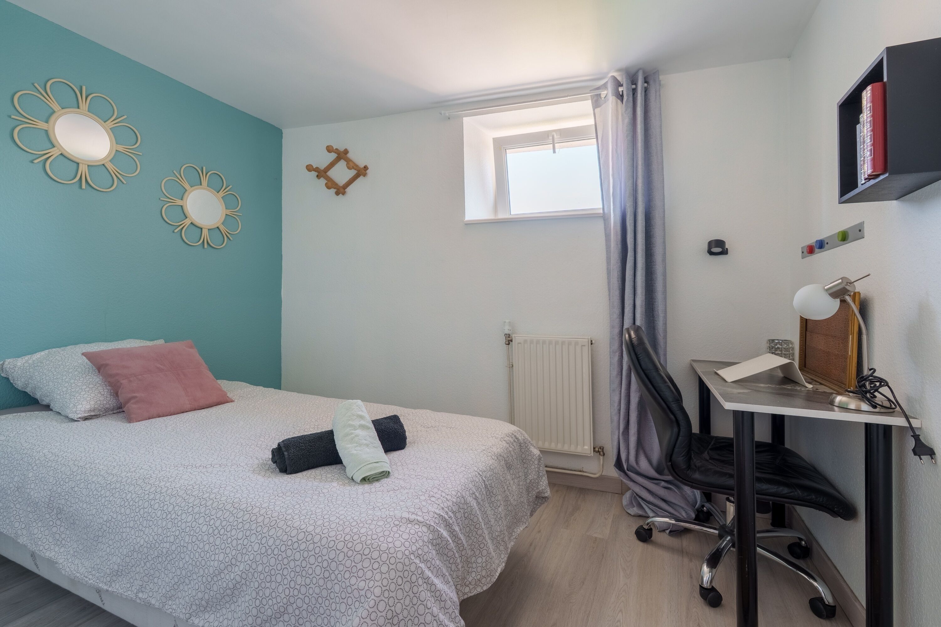 Une chambre à coucher avec un lit, un bureau, une chaise, un radiateur et une fenêtre avec des rideaux.