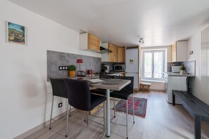 A compact kitchen with modern appliances, a dining area with a table and chairs, and a small window providing natural light. - L’éclat de Baccarat - Maison cosy en triplex (Baccarat)