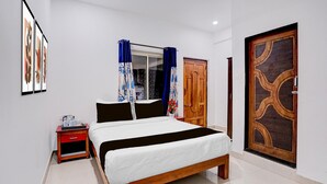 Une chambre à coucher comprenant un lit, une table de chevet, une fenêtre avec des rideaux, une porte en bois et une œuvre d’art accrochée au mur.