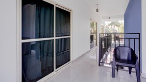 Un couloir avec une grande porte-fenêtre coulissante, une chaise en plastique noire et un balcon doté d’une rambarde en métal.