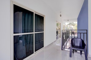 A corridor with a large sliding glass door, a black plastic chair, and a balcony with a metal railing. - Suite With Balcony Ravai (Calangute)