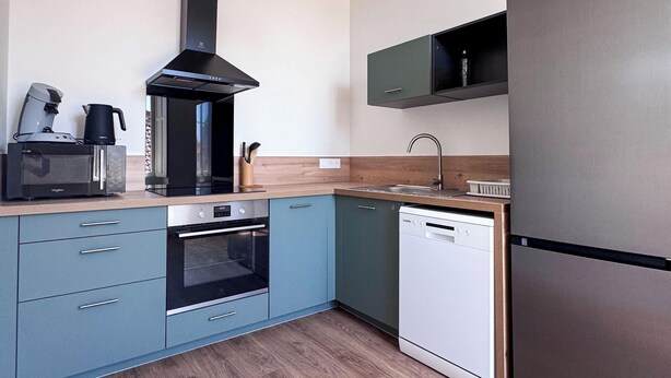 A modern kitchen with a built-in oven, microwave, and dishwasher, a coffee maker, and a hanging light fixture. - Tranquiloue - Appart Centre-Ville 20min Puy du Fou (Les Herbiers)