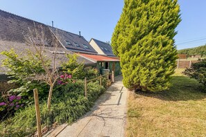Ein Weg führt zu einem Haus mit einem geneigten Dach, einem Holzzaun und einem hohen Nadelbaum.