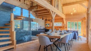Ein modernes Interieur aus Holz mit Essbereich, Küche und großen Fenstern.
