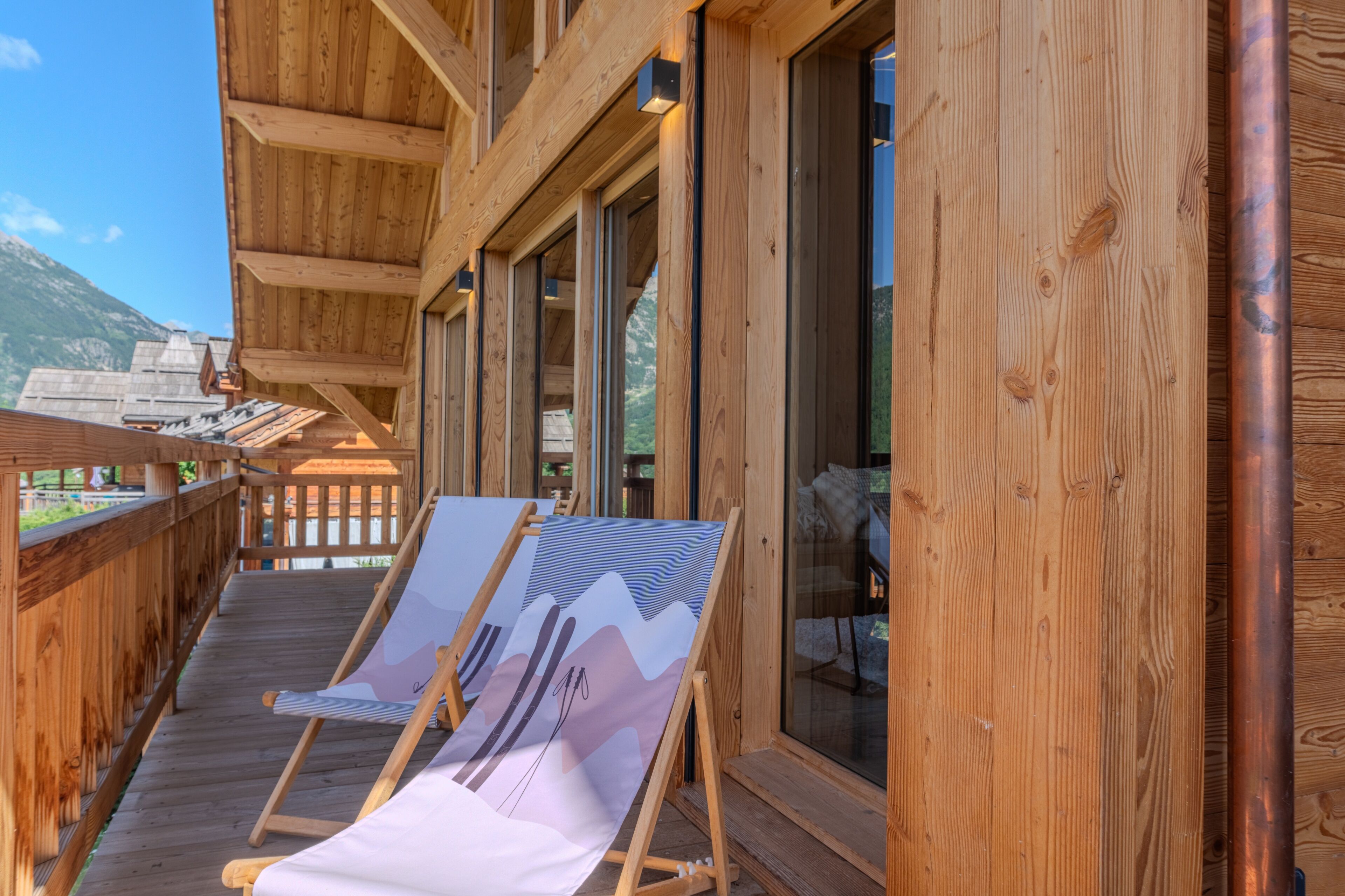 A wooden balcony with a view of mountains, wooden railings, and a glass door.