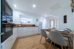 Una cocina moderna con electrodomésticos integrados, un comedor con una mesa y sillas de madera, y un cartel con la palabra 'WELCOME'.