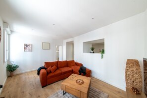 Ein modernes Wohnzimmer mit einem Ecksofa, einem Holztisch und einer kleinen Pflanze auf der Fensterbank.