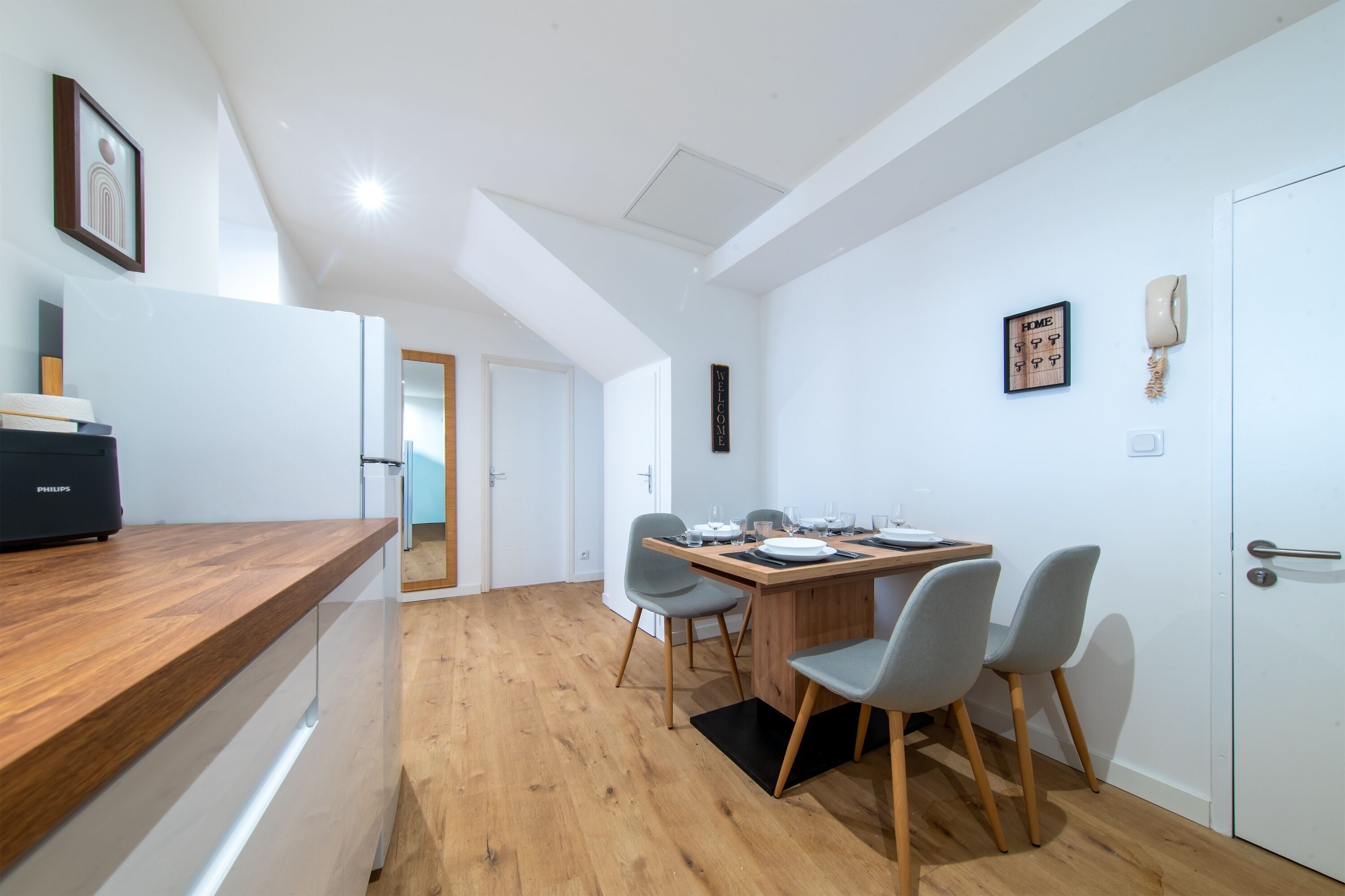 Una cocina moderna con encimera de madera, un refrigerador Philips empotrado y una zona de comedor con mesa de madera y sillas grises.