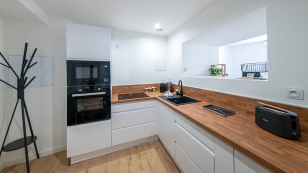 A modern kitchen with white cabinetry, a black microwave, an oven, a wooden countertop, and a black toaster. - Le Cocon du Centre - Appt au cœur de Poitiers (Poitiers)
