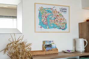 A framed map of Les Sables d'Olonne on a wall, a wicker basket with books, and a white kettle on a shelf. - Le Dombret - Avec vue mer (Les Sables d'Olonne)