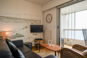 Ein Wohnzimmer mit Sofa, Tisch, Fernseher und Blick ins Freie.