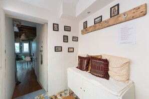Un couloir avec un banc blanc, une étagère en bois ornée de tableaux et un sol carrelé.