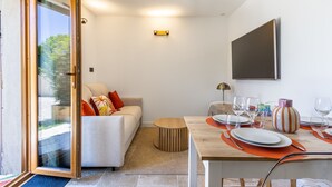 Un salon moderne avec un canapé, une table à manger pour quatre personnes et un grand téléviseur fixé au mur.
