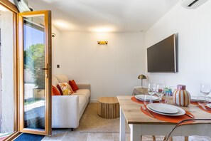 A modern living room with a sofa, dining table set for four, and a large TV mounted on the wall. - L'Ecrin de Capitello - Bel appt proche plage (Grosseto-Prugna)