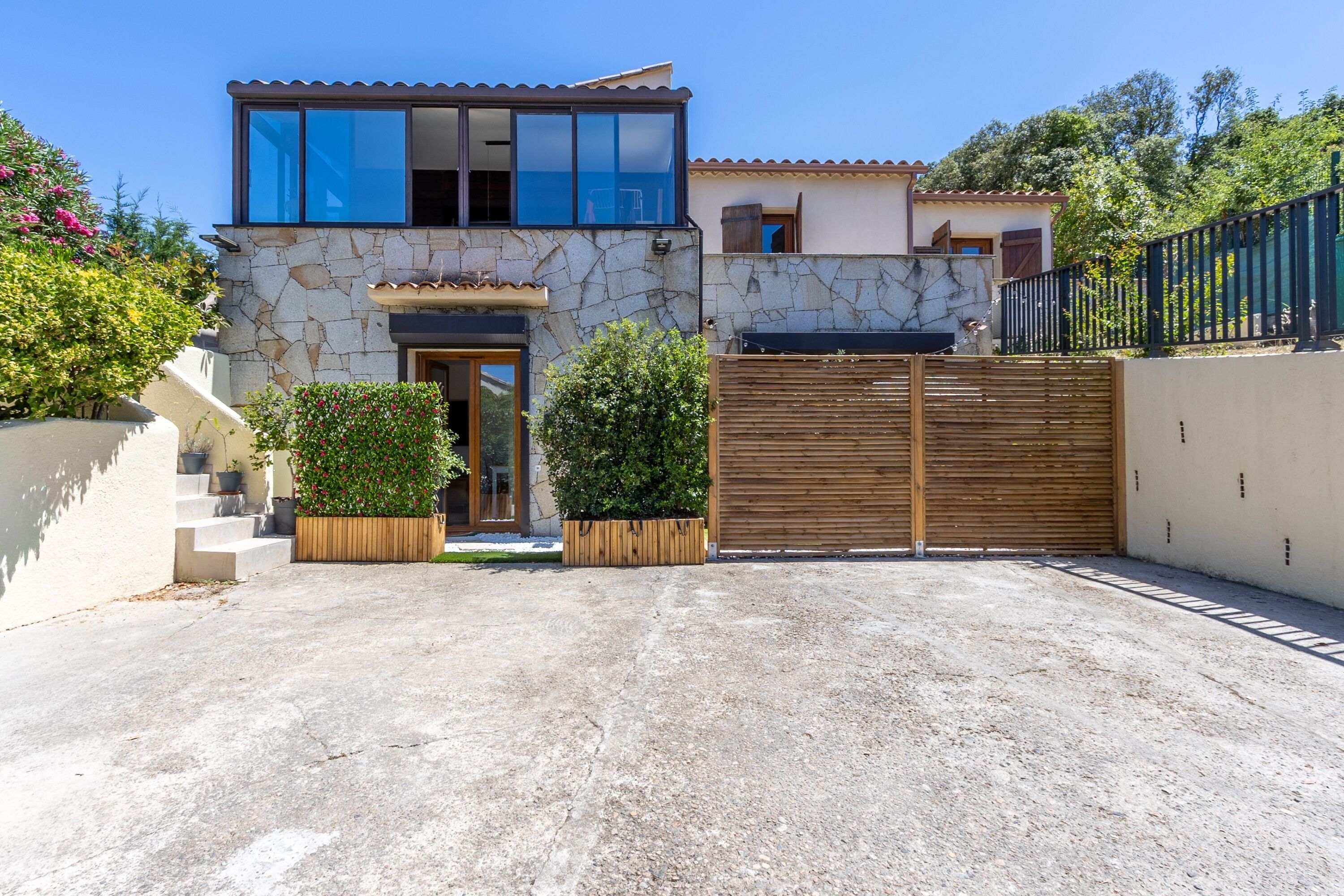 Una casa moderna de dos pisos con fachada de piedra, un portón de madera y un camino de entrada despejado.