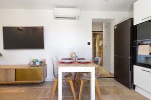 A modern kitchen with a dining area, a black refrigerator, and a mounted flat-screen TV. - L'Ecrin de Capitello - Bel appt proche plage (Grosseto-Prugna)