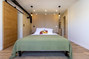 A modern bedroom with a large bed, wooden panel wall, and pendant lighting. - L'Ecrin de Capitello - Bel appt proche plage (Grosseto-Prugna)