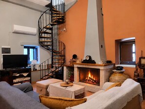 Ett vardagsrum med en öppen spis, en spiraltrappa, en tv och en soffa.