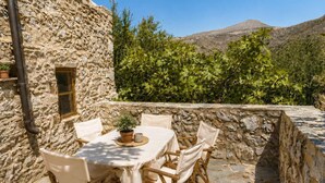 Un espacio de comedor al aire libre con una pared de piedra, una mesa con sillas y vistas a un paisaje montañoso.