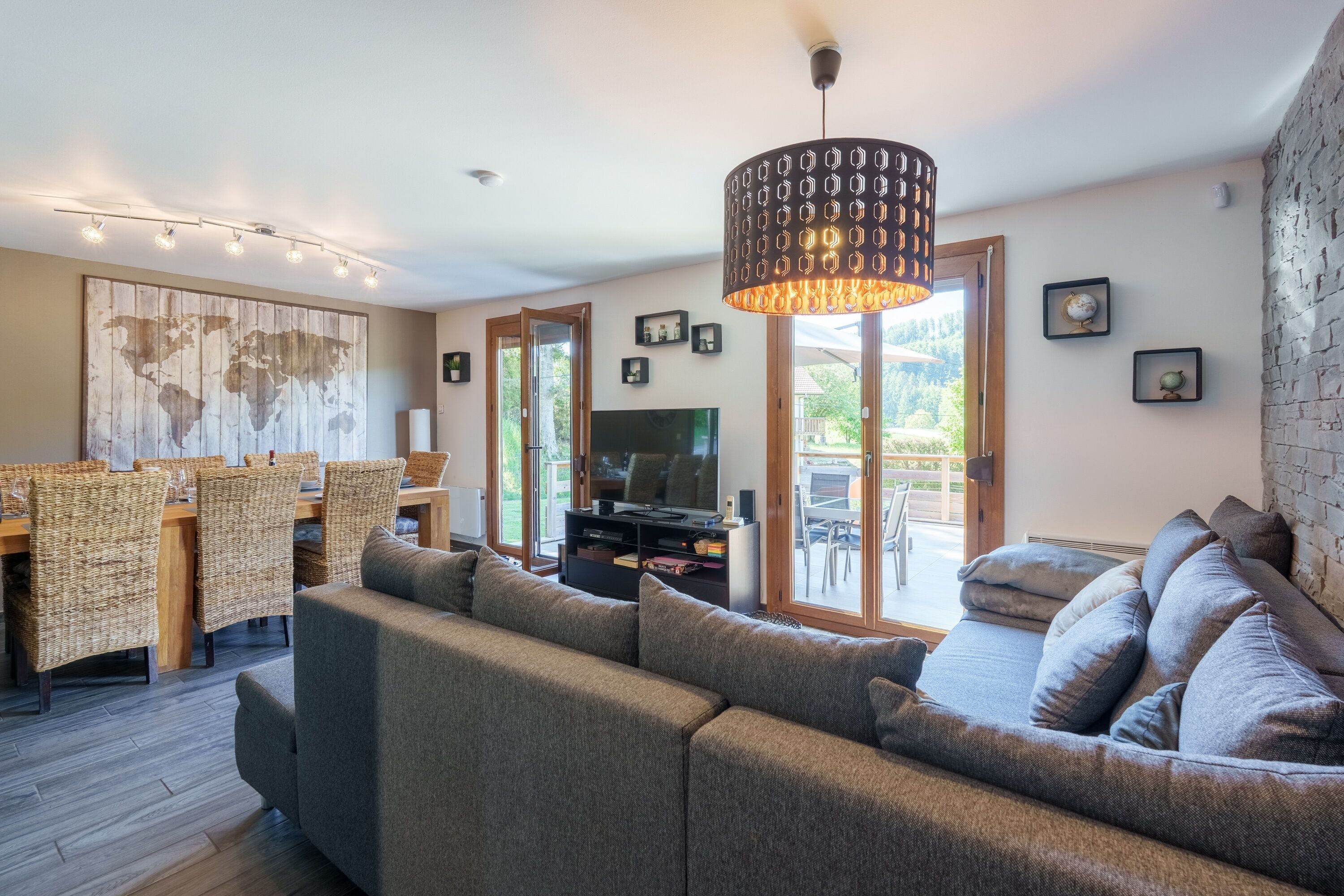 A modern living room with a sofa, television, dining area, and a large world map on the wall.