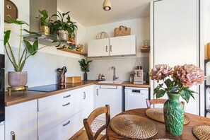 A modern kitchen with white cabinets, a wooden countertop, and a dining area with a wooden table and chairs. - Azur & Magnolia - À 750 m de la plage (La Seyne-sur-Mer)