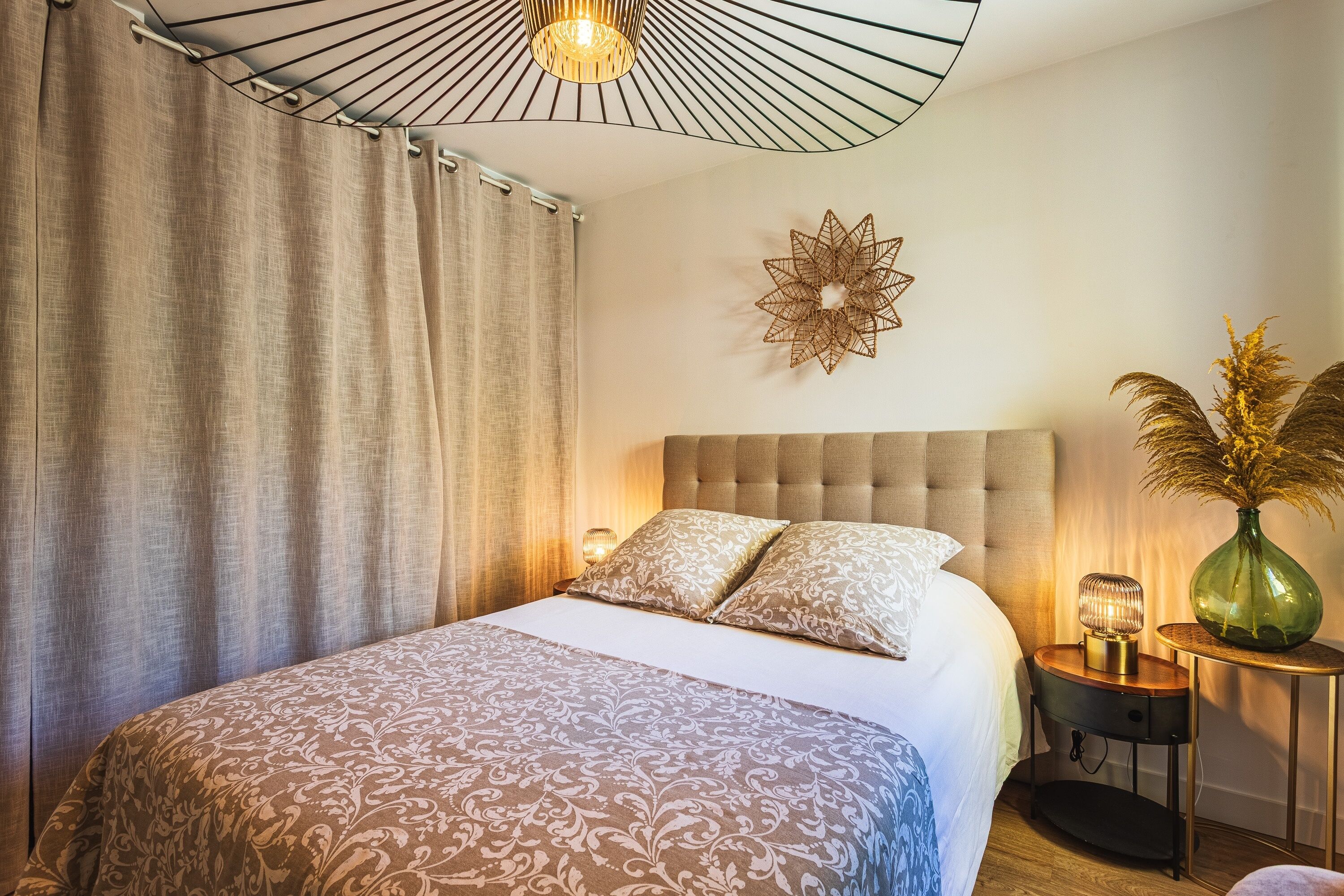 A hotel room with a large bed, a nightstand, a wall-mounted lamp, and a decorative wall piece.