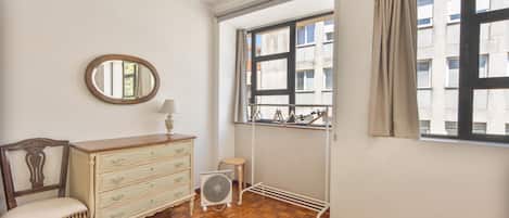 Una habitación con cómoda de madera, una silla, un radiador y una ventana con cortinas.