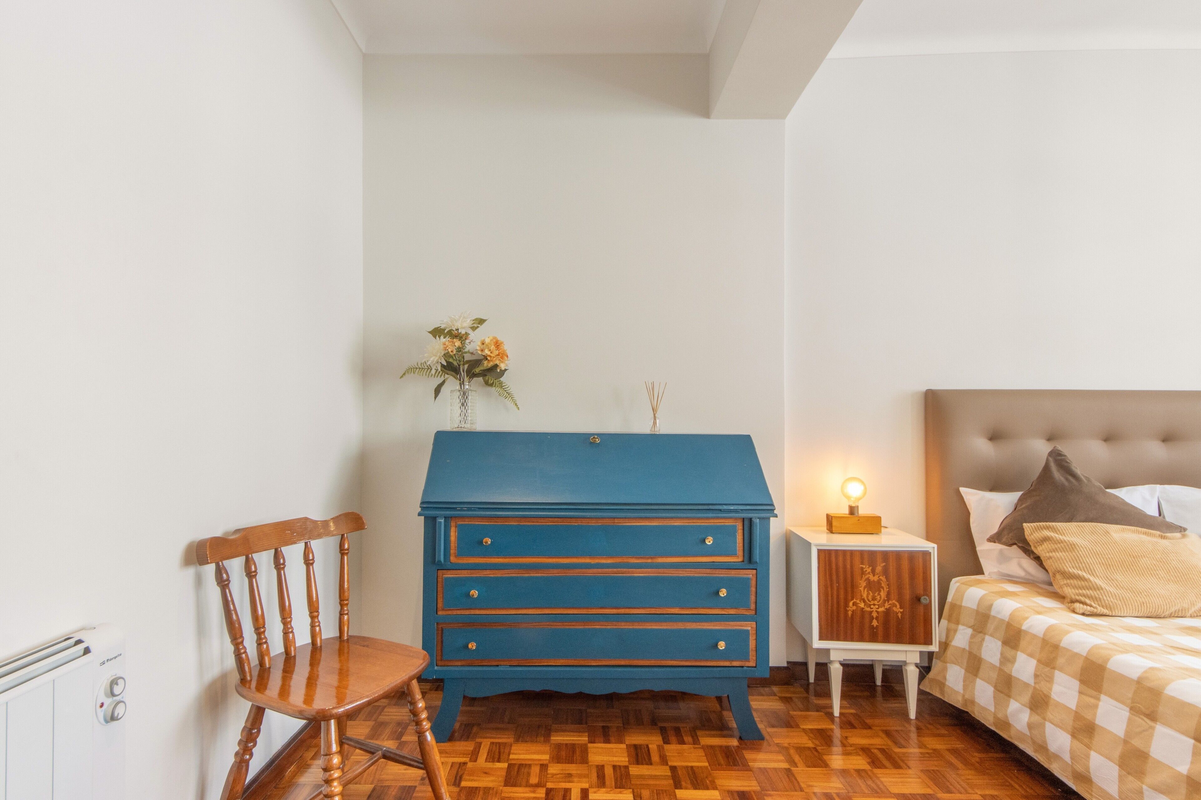 Une chambre à coucher comprenant un lit, une commode, une chaise et une table de chevet avec une lampe.