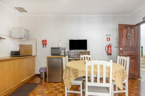 Cuina compacta amb microones, torradora i nevera petita. Hi ha una taula de menjador amb cadires i un televisor.